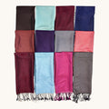 A set of twelve folded fabric scarves or wraps arranged in a 3-by-4 grid on a plain light background. The top scarf has fringe at the top edge and displays a variety of colors including burgundy, light blue, magenta, taupe, terracotta, purple, gray, coral pink, brown, mint, burgundy, and navy blue.