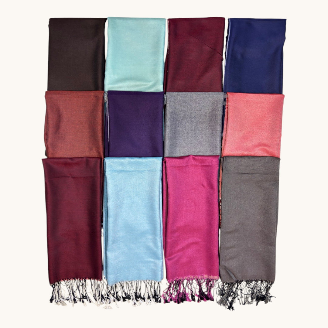 A set of twelve folded fabric scarves or wraps arranged in a 3-by-4 grid on a plain light background. The top scarf has fringe at the top edge and displays a variety of colors including burgundy, light blue, magenta, taupe, terracotta, purple, gray, coral pink, brown, mint, burgundy, and navy blue.