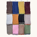 Twelve folded knit scarves or wraps in assorted colors, hanging from white plastic hangers against a plain off-white background. The colors include brown, blue, mustard yellow, burgundy, light gray, orange, charcoal, pale pink, taupe, green, light brown, and dusty blue.