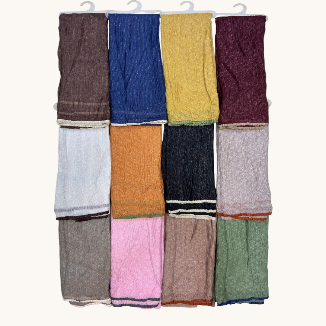 Twelve folded knit scarves or wraps in assorted colors, hanging from white plastic hangers against a plain off-white background. The colors include brown, blue, mustard yellow, burgundy, light gray, orange, charcoal, pale pink, taupe, green, light brown, and dusty blue.