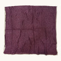 A square piece of textured purple fabric with a frayed, raw edge, laid flat against a light off-white background.