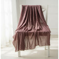A dusty rose textured cotton muslin throw blanket draped over a white wooden chair in a bright, sunlit room.