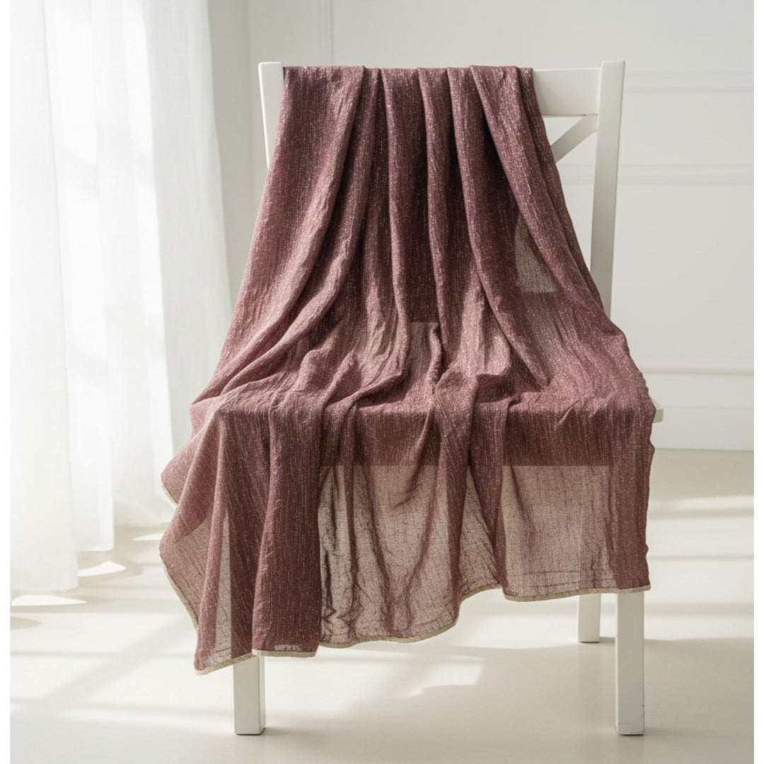 A dusty rose textured cotton muslin throw blanket draped over a white wooden chair in a bright, sunlit room.