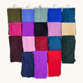 A set of folded colorful fabric scarves or wraps arranged in a grid on a white wall with metal hooks below. The collection includes multiple colors such as purple, red, blue, pink, green, black, and beige.