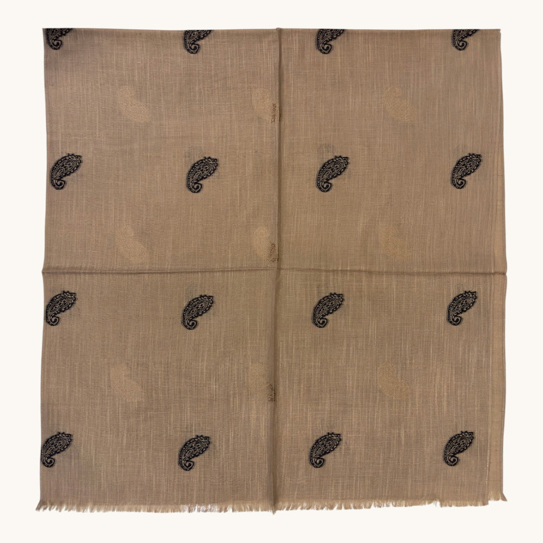 A beige woven textile with a subtle sheen and small black paisley motifs repeated across the surface, shown flat against a plain light background.