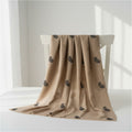 A beige draped scarf with a repeating black paisley pattern, displayed on a white wooden chair in a bright, minimalist room.