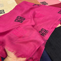 A close-up of a bright pink woven scarf with black geometric logos, held by a hand to show its texture and fringed edges.