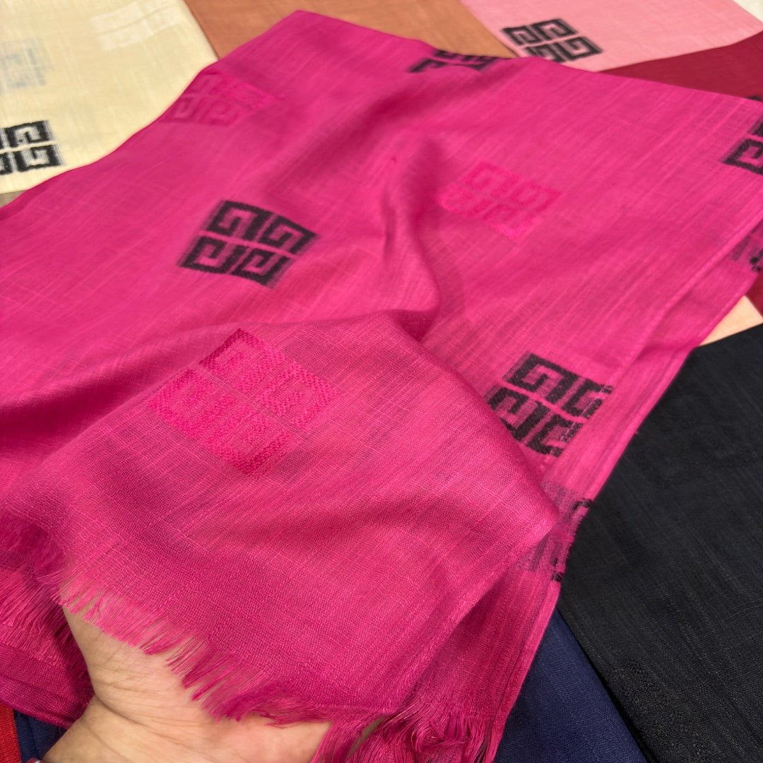 A close-up of a bright pink woven scarf with black geometric logos, held by a hand to show its texture and fringed edges.