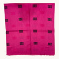 A bright pink woven textile, likely a scarf or sari, featuring a repeating pattern of black Greek key motifs and subtle pink medallions on a light beige background.