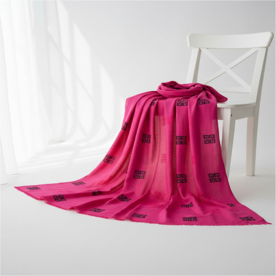A bright pink shawl with black geometric patterns draped over a white wooden chair in a bright, minimalist room.
