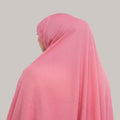 A pink textured crinkle gauze hijab worn by a model, shown from a side-back angle against a solid light gray background.