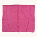 A bright pink crinkled fabric square, likely a scarf or handkerchief, laid flat against a light cream background.