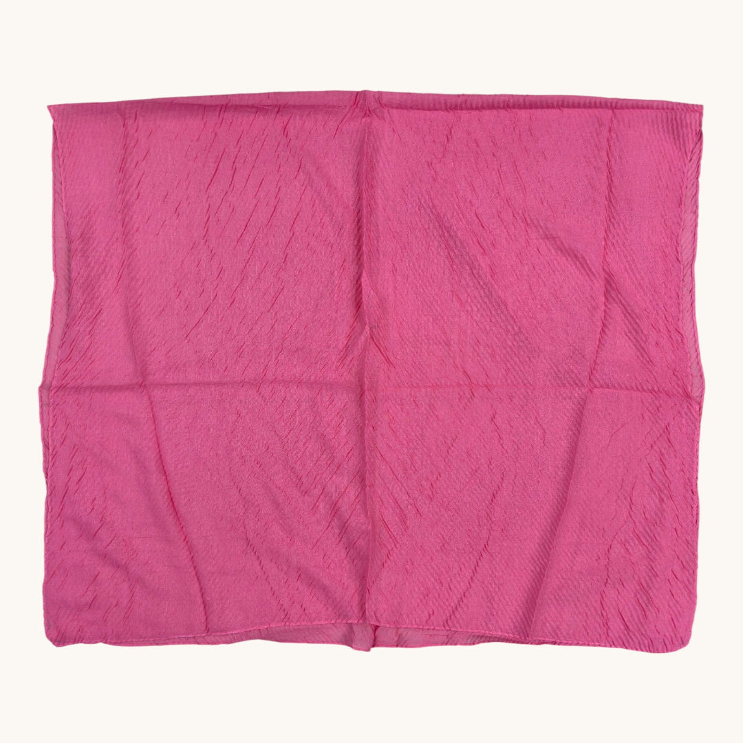 A bright pink crinkled fabric square, likely a scarf or handkerchief, laid flat against a light cream background.