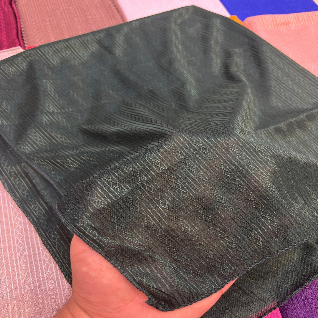 A close-up of a dark charcoal gray textured fabric square being held by a hand, showing a woven geometric pattern.