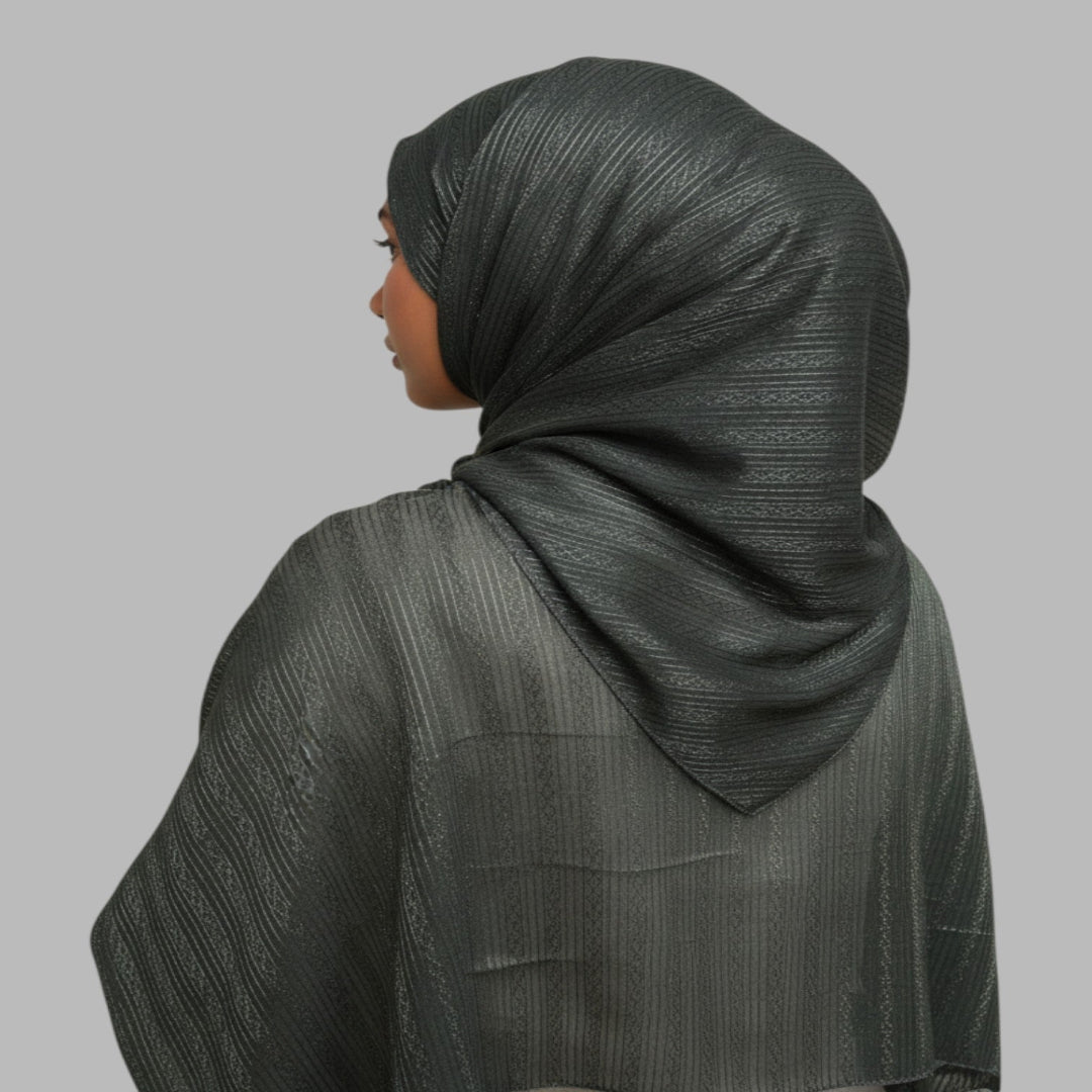A woman shown from the back wearing a dark gray textured hijab and matching draped shawl against a solid gray background.