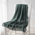 A dark green textured throw blanket draped over a white wooden chair in a bright, minimalist room.