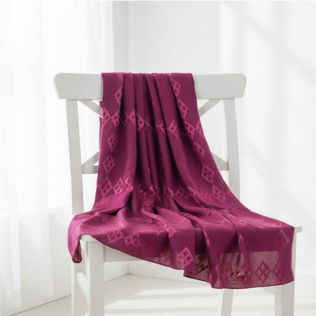 A magenta purple patterned scarf draped over a white wooden chair in a bright, minimalist room.