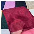 A close-up of a hand holding a folded deep red woven scarf with a subtle geometric pattern, with other color options of the scarf visible in the background.