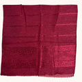 A deep red woven textile, likely a scarf or shawl, featuring horizontal bands of a Greek key pattern and small floral motifs, finished with a fringed edge.