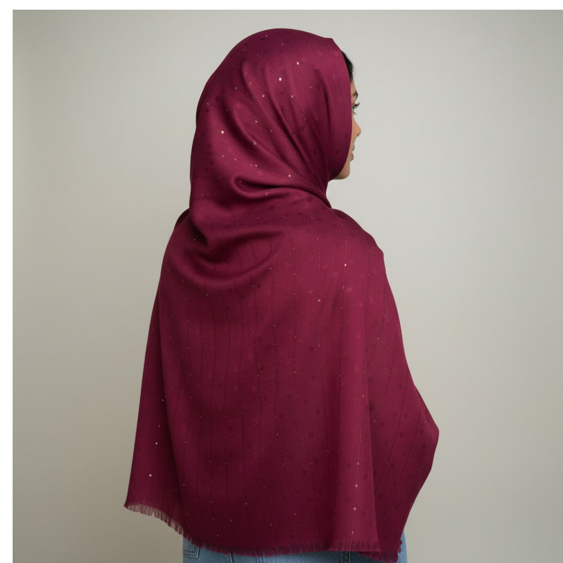 A woman shown from the back wearing a deep burgundy hijab with subtle silver glitter accents, set against a plain light gray background.