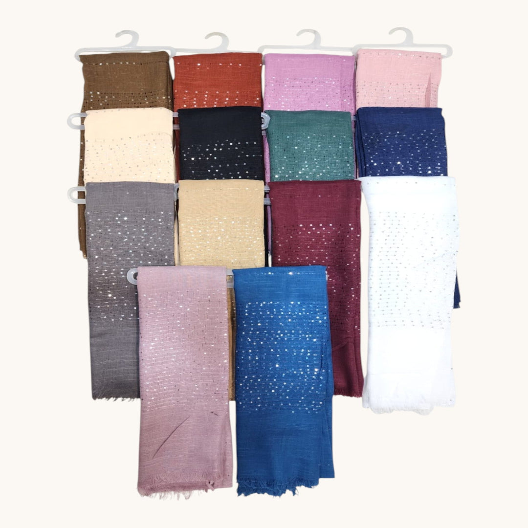 A set of 18 folded cotton scarves in various colors, featuring a traditional eyelet or embroidered pattern, hanging on white plastic hangers against a light cream background.